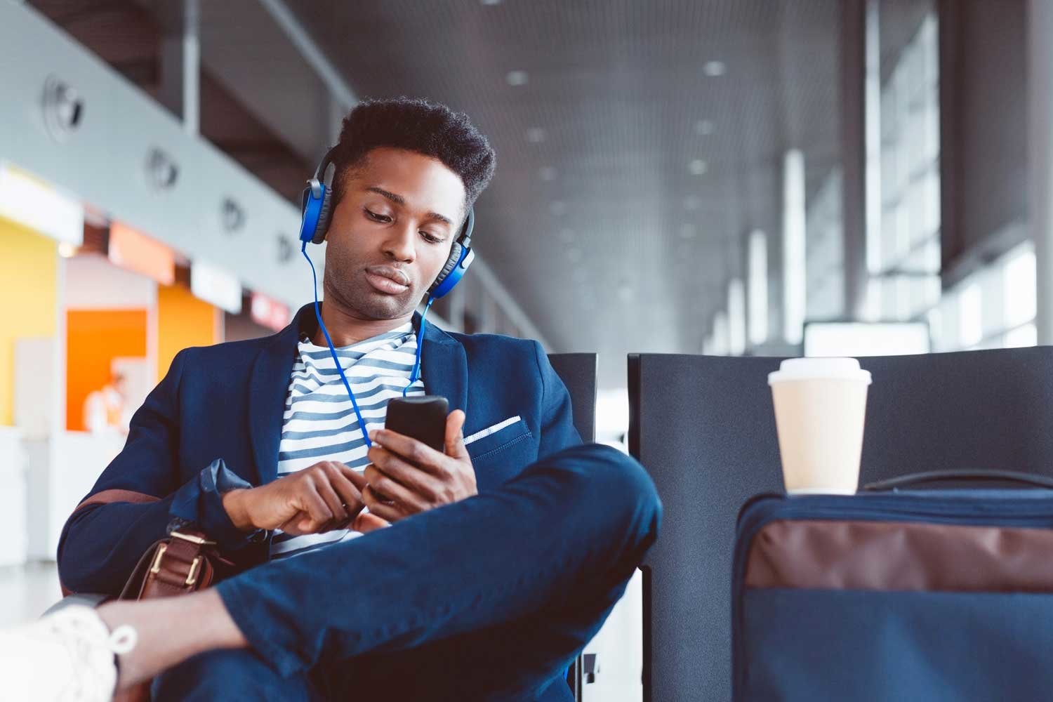 Shot of young african man sitting at airport lounge and listening music on mobile phone while waiting for flight